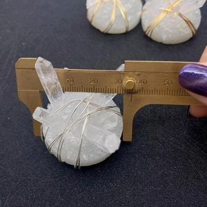 Macro shot measuring the white crystal pendant with silver wire wrap using a brass caliper