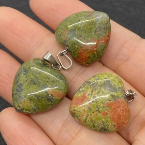 Drie hartvormige Unakite steen hangers met natuurlijke groene en oranje patronen op een palm