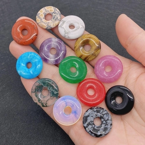 Makroansicht von 13 bunten Naturstein-Anhängern in einer Hand für DIY-Schmuckzubehör