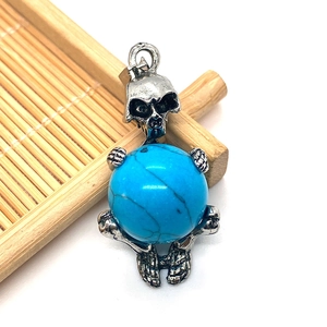 Detailed macro view of a skull-shaped pendant holding a turquoise bead on bamboo texture