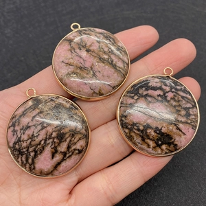 Trois pendentifs ronds en pierre naturelle rose et noire avec bord doré tenus en main