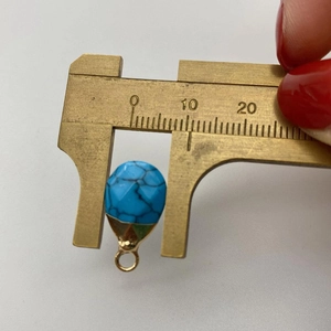 Close-up measurement of blue faceted teardrop pendant with gold base and caliper