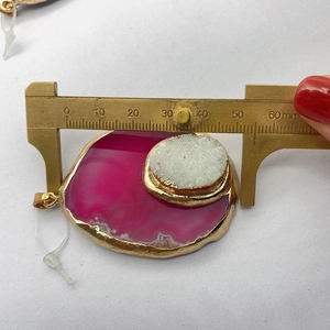 Detailopname van de meting van een roze agaat hanger met een messing schuifmaat