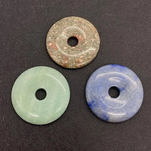 Detailed view of three polished 50mm natural stone donut pendants in green and blue tones