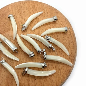 Polished natural shell chili-shaped pendants with silver caps on a round wooden tray