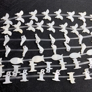 Macro detail of hand-carved white shell charms in bird and butterfly shapes for DIY jewelry