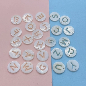 Detailed macro view of 12mm flat round shell beads with hollow alphabet letter carvings