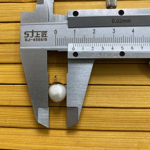 Caliper measuring the 12mm width of a natural freshwater pearl pendant with gold cap