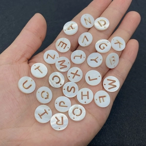 Hand holding natural 12mm shell alphabet beads with hollowed letters for DIY jewelry