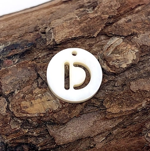 Gros plan d'un pendentif rond en nacre blanche avec lettre D ajourée sur fond d'écorce