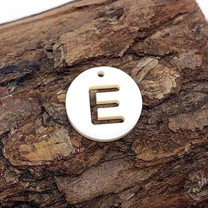 Vue macro d'un pendentif en coquillage blanc avec lettre E évidée sur écorce