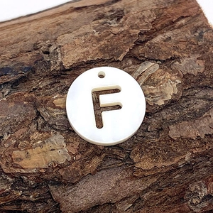 Vue détaillée du pendentif en nacre naturelle lettre F sur un fond d'écorce rustique