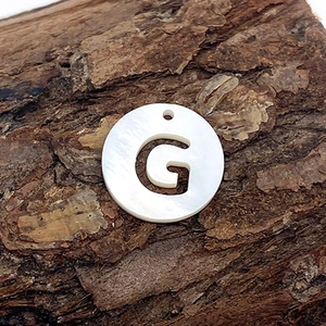 Vue macro d'un pendentif en nacre naturelle avec lettre G ajourée sur support écorce