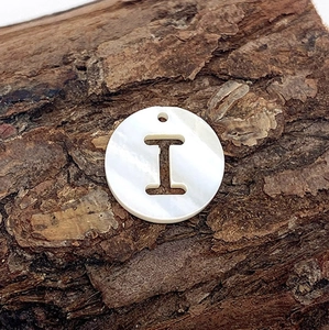 Détail macro d'un pendentif en nacre naturelle avec la lettre I ajourée et reflets nacrés