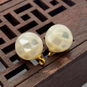 Macro shot of mosaic shell bead charms with white checkerboard texture and gold loop