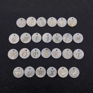 Macro detail of 26 round white shell pendants with golden letters for DIY necklaces