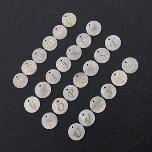 Flat lay of circular white mother of pearl pendants with gold cursive initial letters