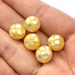 Détail macro de perles en nacre mosaïque jaune et blanche tenues en main pour bijoux DIY