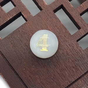 Macro shot of circular white shell bead with gold number four for DIY jewelry