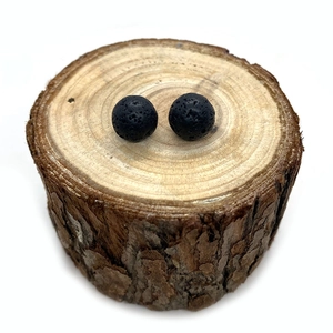 Dettaglio macro di due perle di pietra lavica nera porosa su una fetta di legno rustico