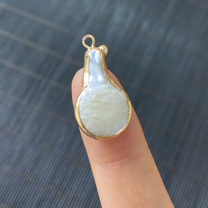 Colgante de perla barroca de agua dulce con borde dorado mostrado en la punta del dedo