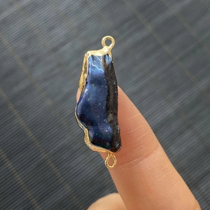 Connecteur perle bleu foncé irrégulier avec bord doré tenu entre doigts pour la taille