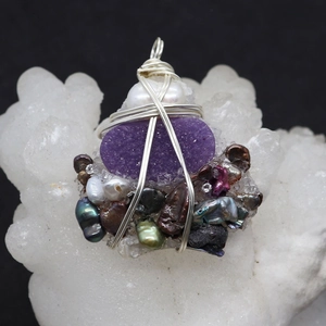 Macro detail of handmade wire wrapped pendant with purple druzy and baroque pearls