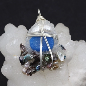 Macro detail of handmade silver wire wrapped natural pearls and blue crystal pendant
