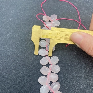 Measuring 10mm pink rose quartz teardrop loose beads with yellow calipers on gray mat