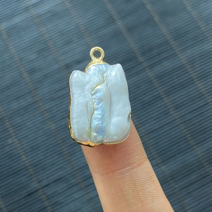 Baroque natural freshwater pearl pendant with gold plating shown on fingertip for scale