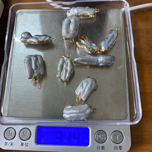 Macro shot of eight grey baroque pearl pendants with gold edges on a digital scale