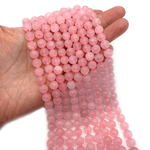 Hand holding strands of natural pink rose quartz round beads for DIY jewelry making