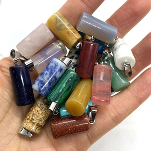 Detailed view of assorted cylindrical natural stone pendants held in hand for scale