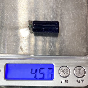 Macro shot of a dark blue cylindrical blue sandstone pendant weighing 4.57g on a scale