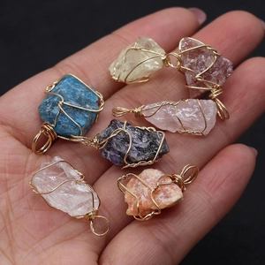 Handheld view of six raw natural crystal pendants with intricate gold wire wrapping details