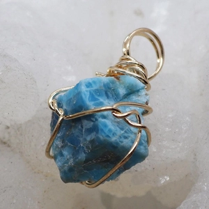 Macro view of handmade wire wrapped blue raw stone pendant with gold finish detailing