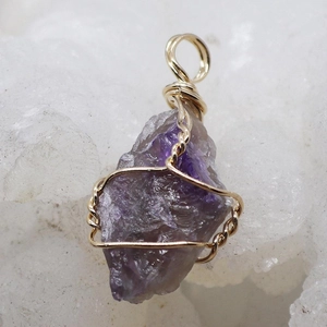 Macro shot of irregular raw amethyst pendant with handcrafted gold wire wrapping detail