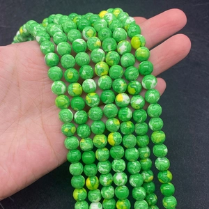Detailaufnahme von grünen Kaisersteinperlen mit Marmorstruktur in der Hand für DIY-Schmuck