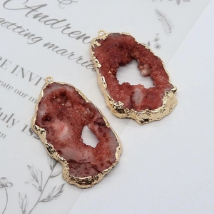 Macro detail of irregular red crystal pendants with gold plated edges on paper