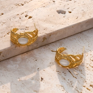 Détail de boucles d'oreilles plume dorée avec incrustation de pierre blanche ovale