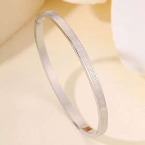 Macro view of silver stainless steel bangle featuring an intricate Greek meander pattern