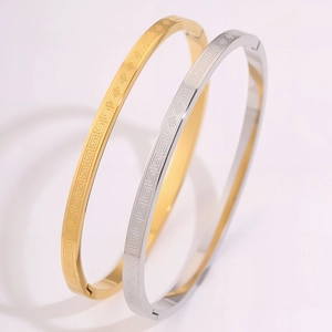 Detail of gold and silver steel bangles featuring classic Greek meander pattern and clasp