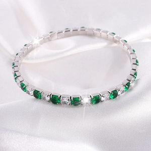 Vista macro de pulsera tenis de cristal con esmeraldas verdes y diamantes sobre seda blanca