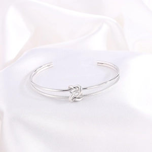 Detalle del brazalete abierto con nudo plateado y texturas metálicas pulidas y trenzadas