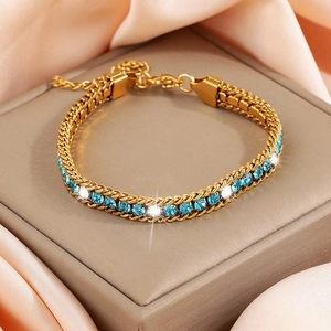 Dettaglio del bracciale dorato in acciaio inossidabile con cristalli blu su seta rosa