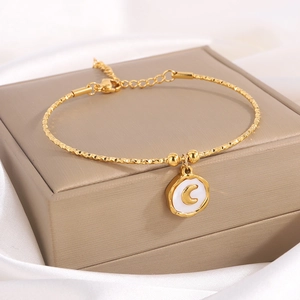 Elegante pulsera de acero de titanio dorado con dije de luna sobre fondo de seda