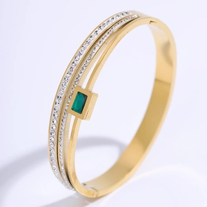 Detail of three-layer gold steel bracelet with emerald green stone and zircon inlay