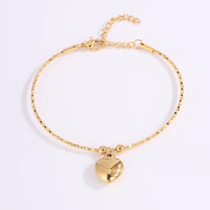 Detalle del colgante de corazón dorado y cadena diamantada en pulsera de acero