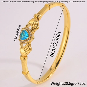 Detailed view of gold bangle featuring heart-shaped blue gemstone and crystal inlay