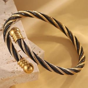 Détail d'un bracelet câble torsadé en acier doré et noir avec extrémités sphériques